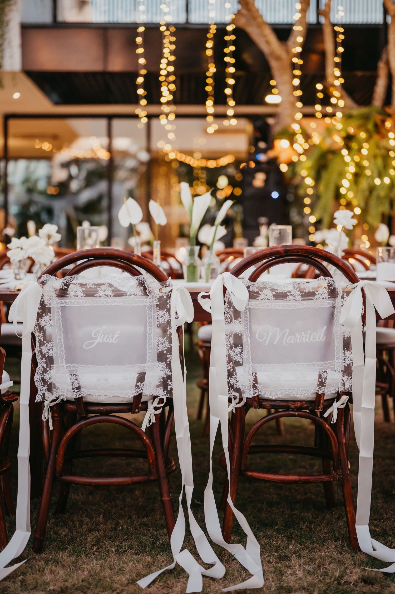 Elegant wedding reception chairs labeled Just Married adorned with white ribbons under warm string lights.