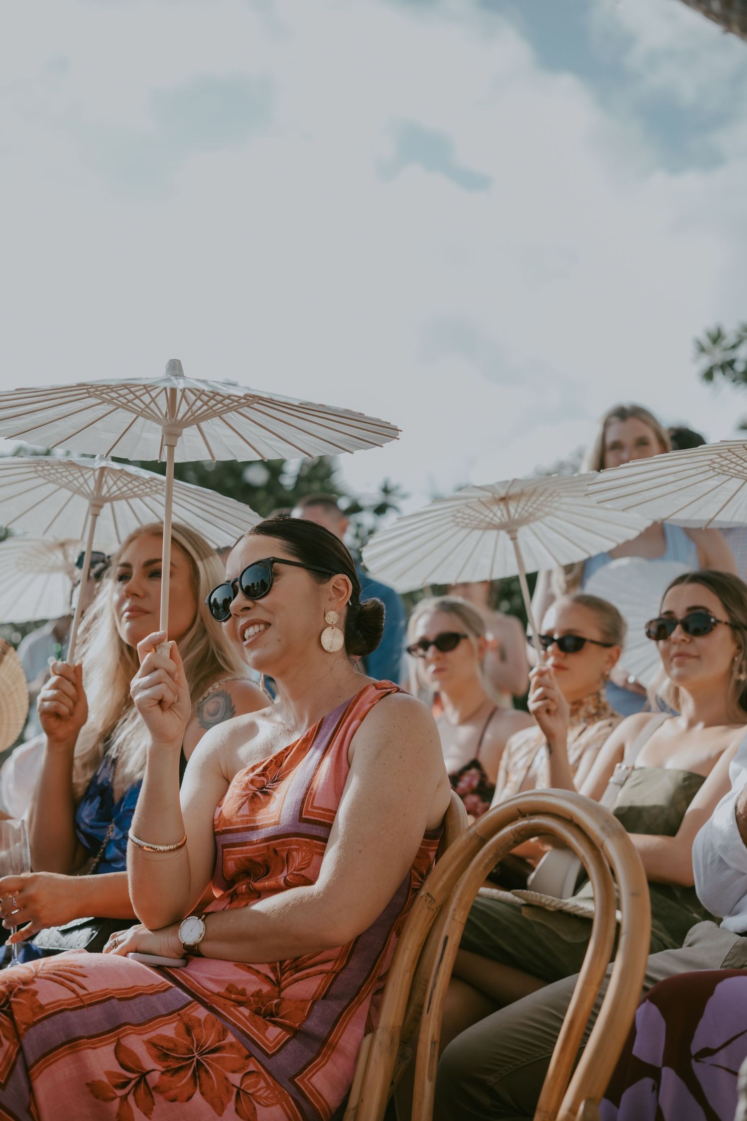 Guests shielding themselves with white parasols while watching an outdoor wedding ceremony.