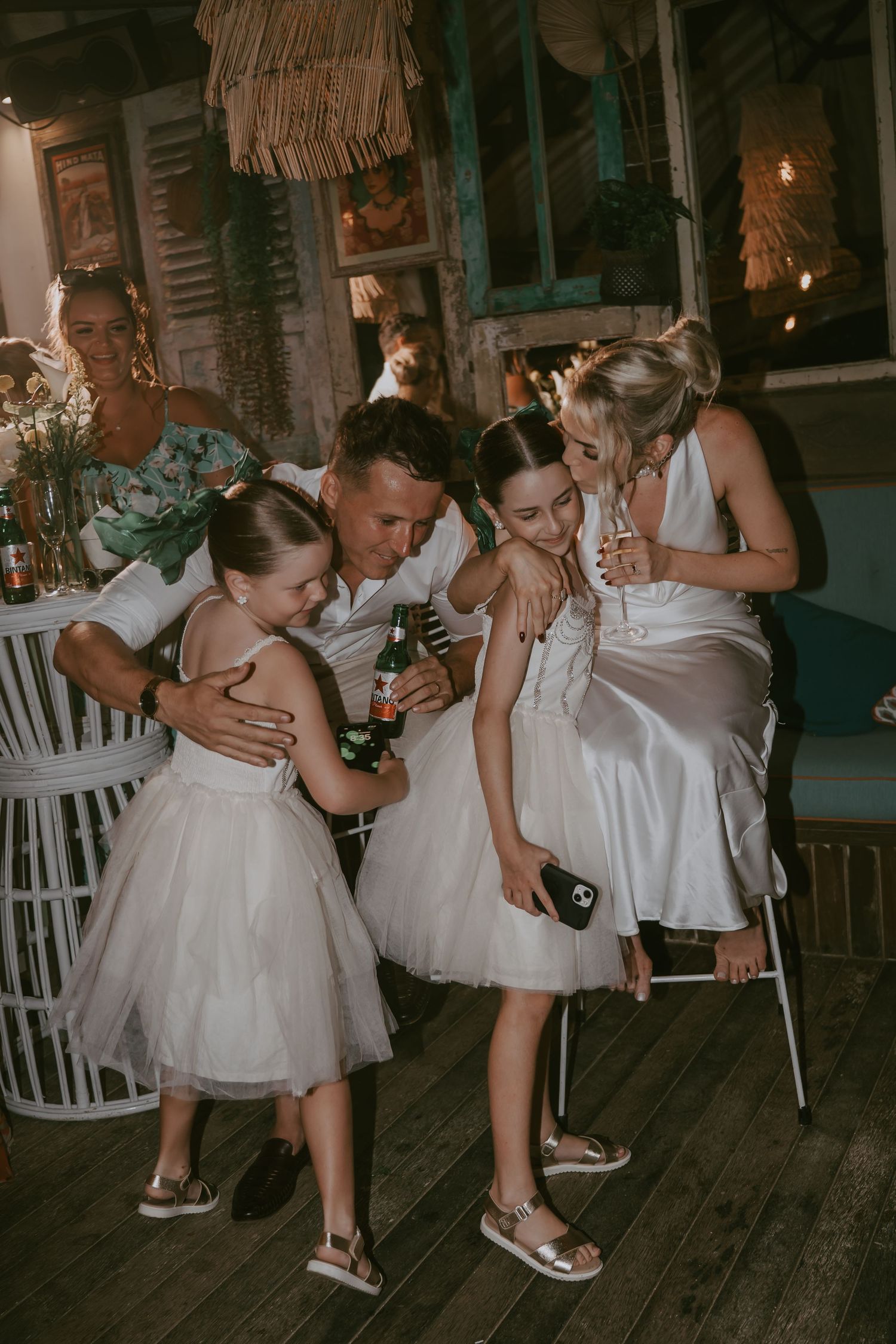 Wedding party members share a candid moment in white dresses during a reception celebration.