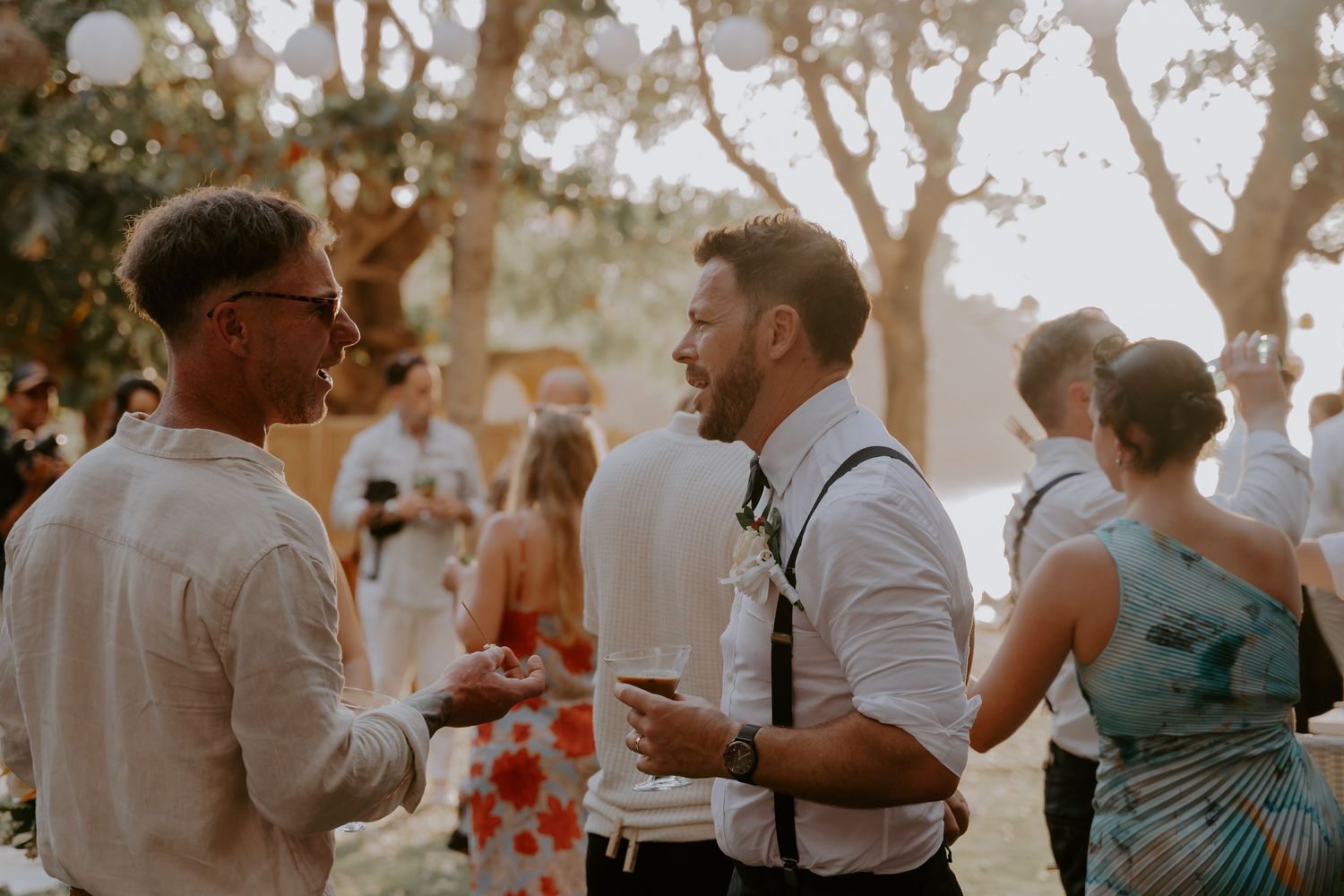 Wedding guests dance and celebrate together during an outdoor reception in warm evening light.