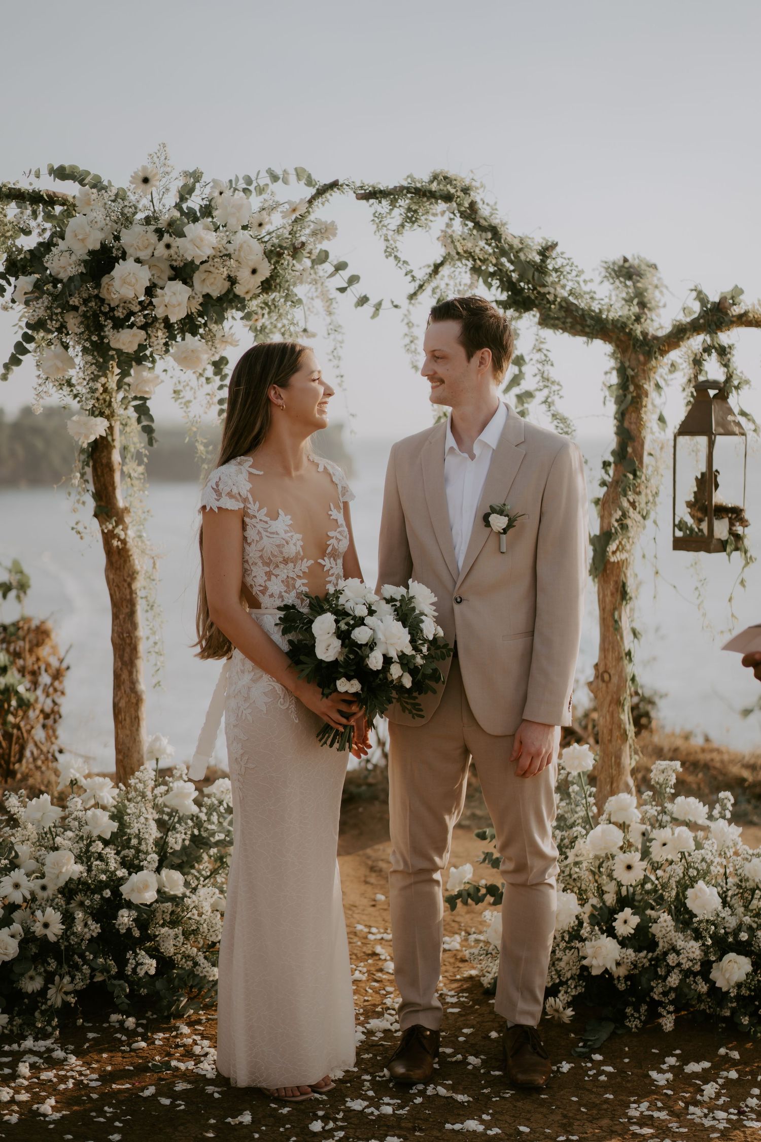A romantic outdoor wedding ceremony under floral-adorned wooden arches with a couple sharing intimate moments.