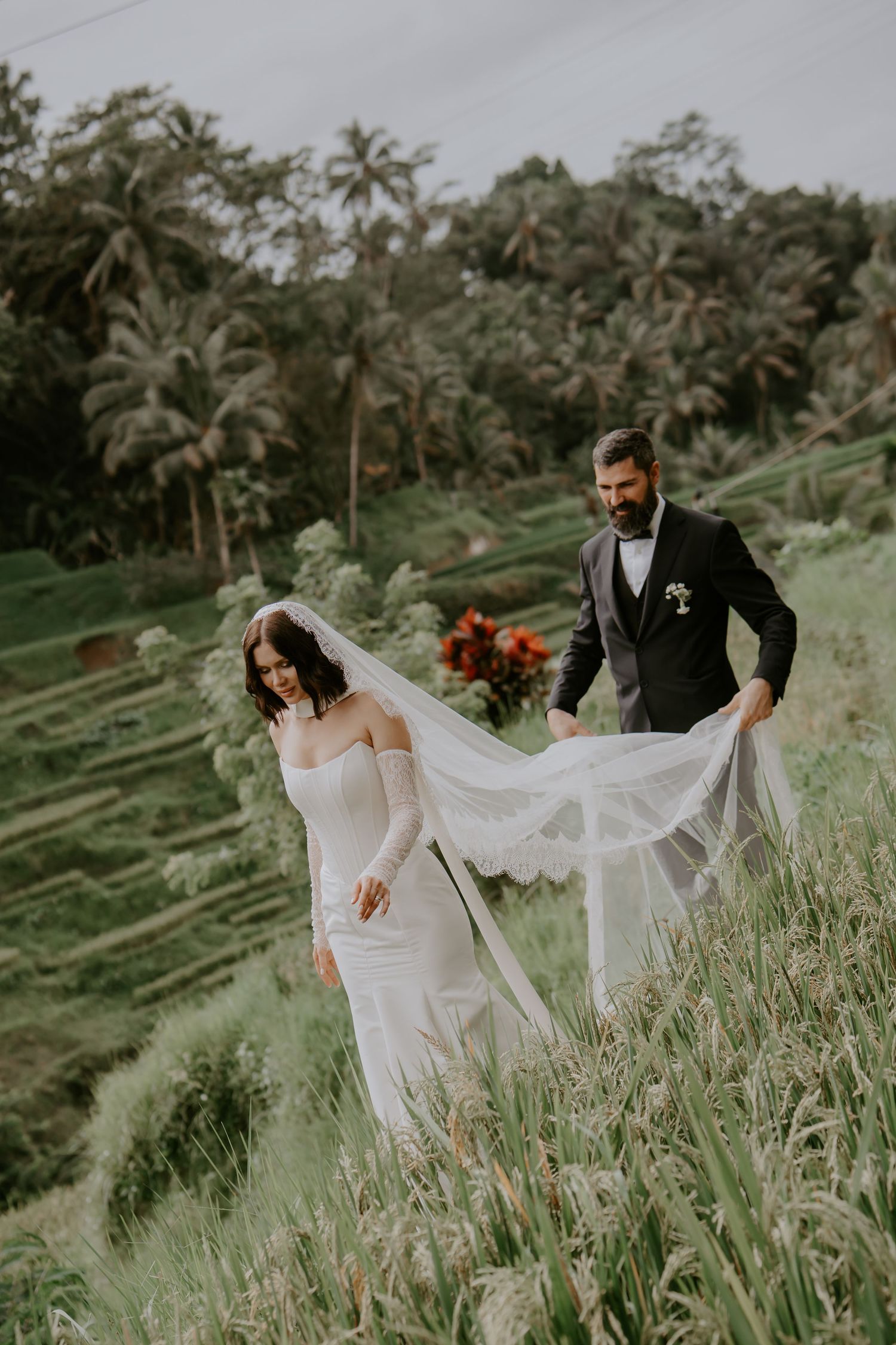 A couple in wedding attire walks through lush green terraced rice fields in Bali during their destination wedding photoshoot.