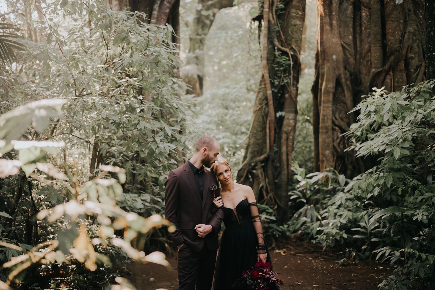Couple in black attire embracing in snowy forest setting with dramatic lighting.