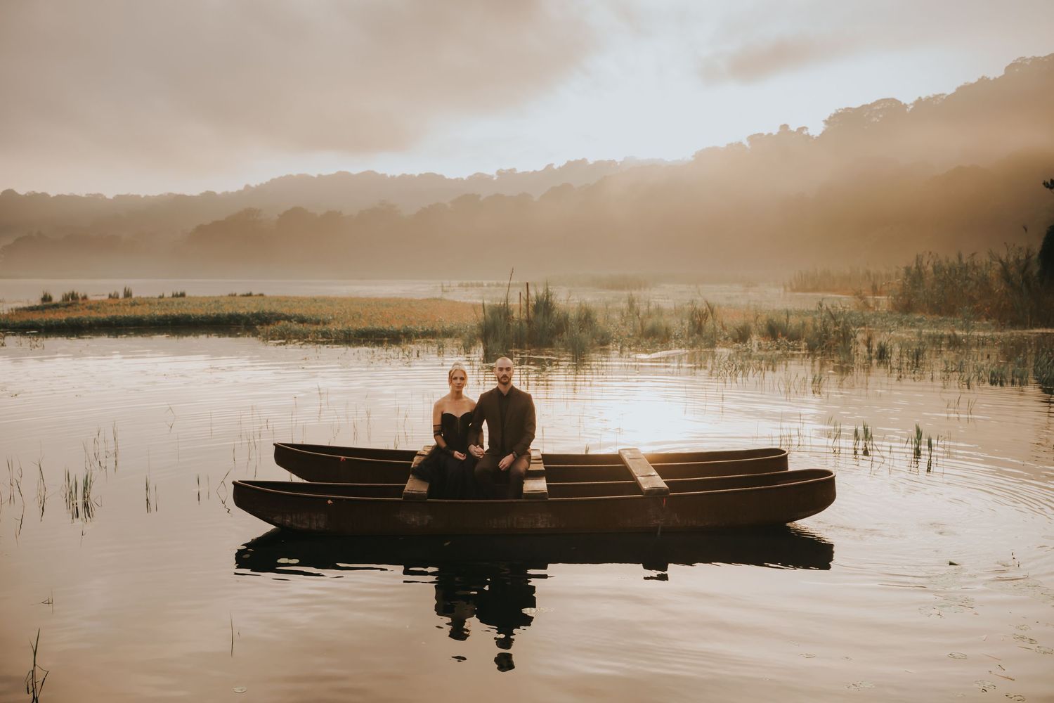 Silhouettes of a couple in a canoe on a serene lake during golden hour.