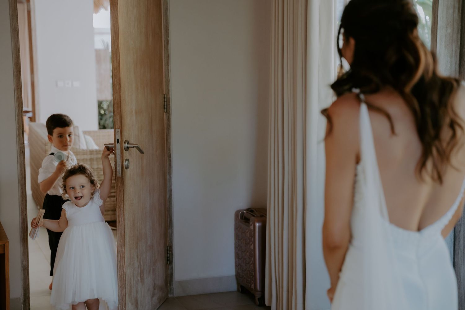 A tender moment during wedding preparations as a bride in white gets ready with help from others in a sunlit room.