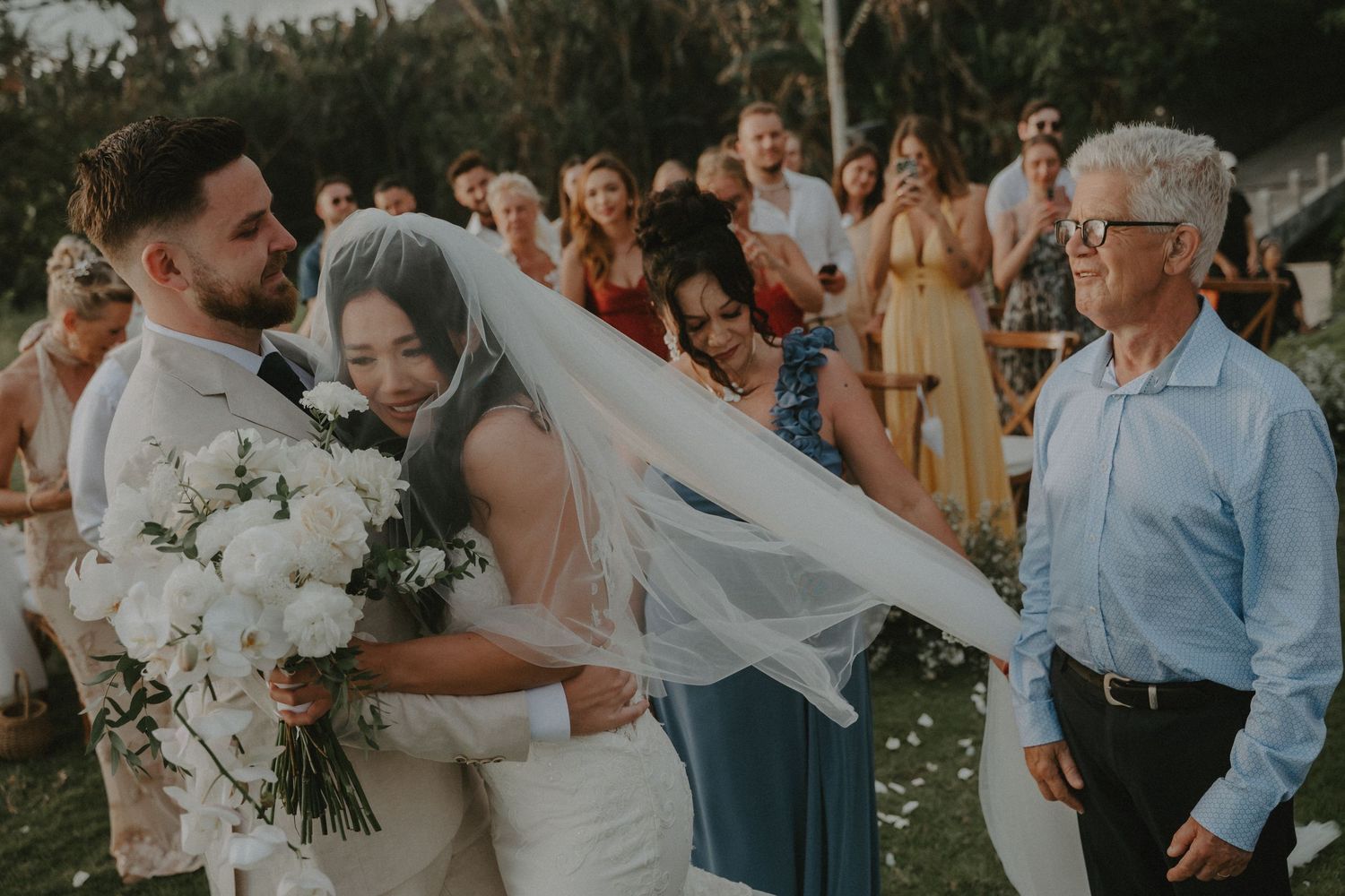 Wedding party celebrates outdoors with guests in casual summer attire.
