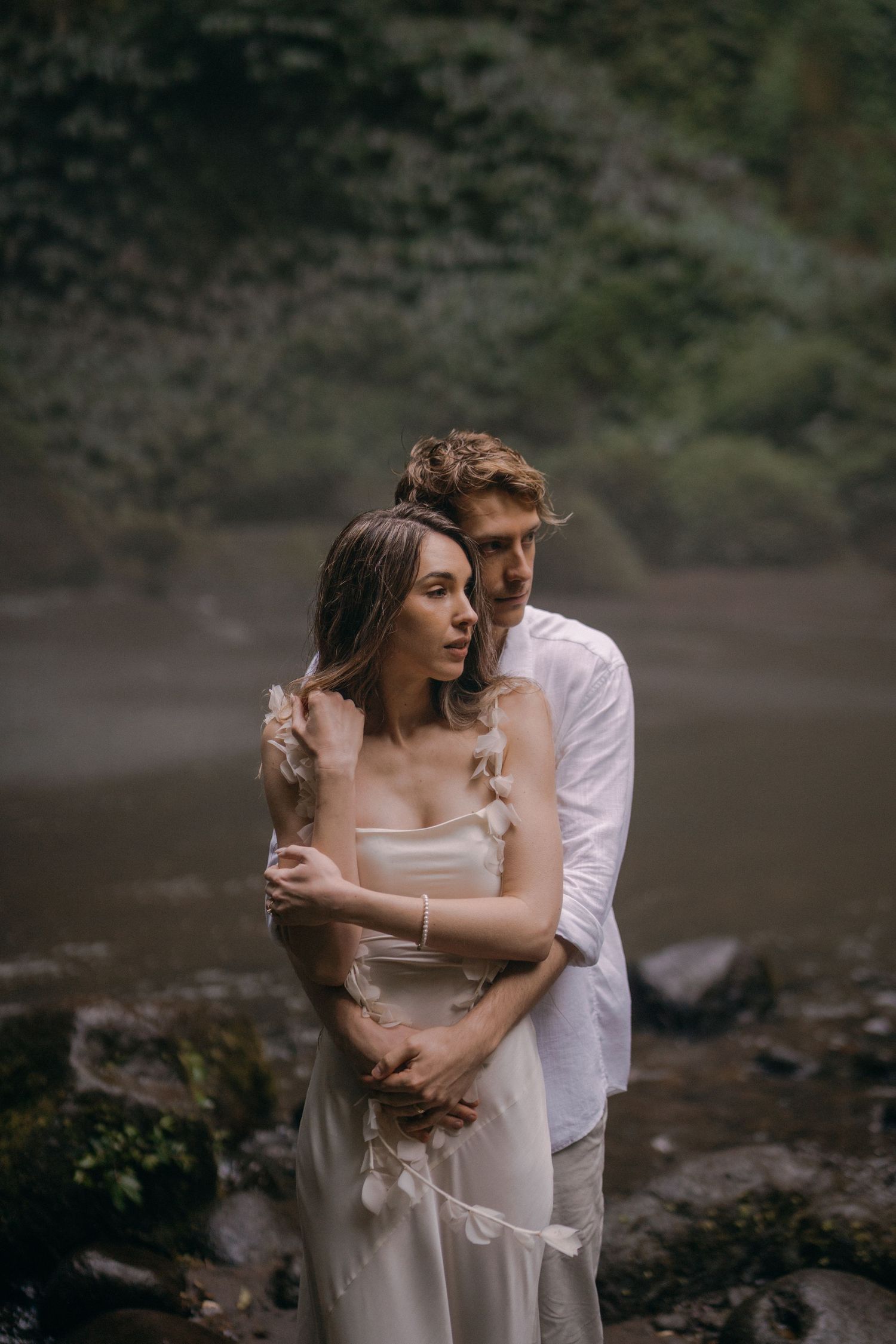 A couple shares an intimate embrace on a rocky beach with moody atmospheric lighting and natural scenery.