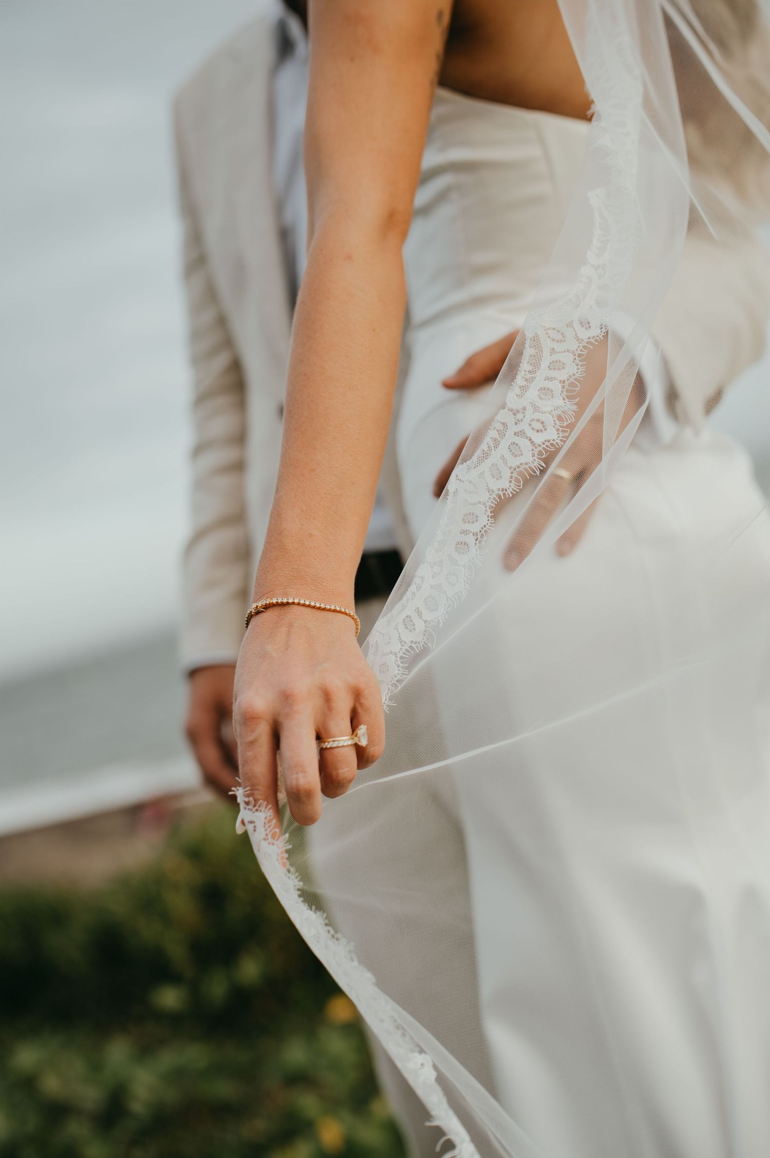Close-up of bride holding wedding dress with gold rings and bracelet visible.