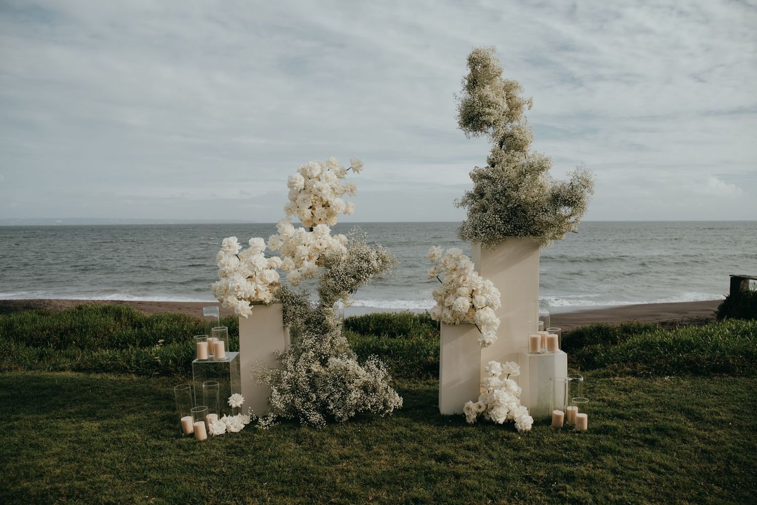 Elegant outdoor beach wedding ceremony arch with white floral arrangements and candles.