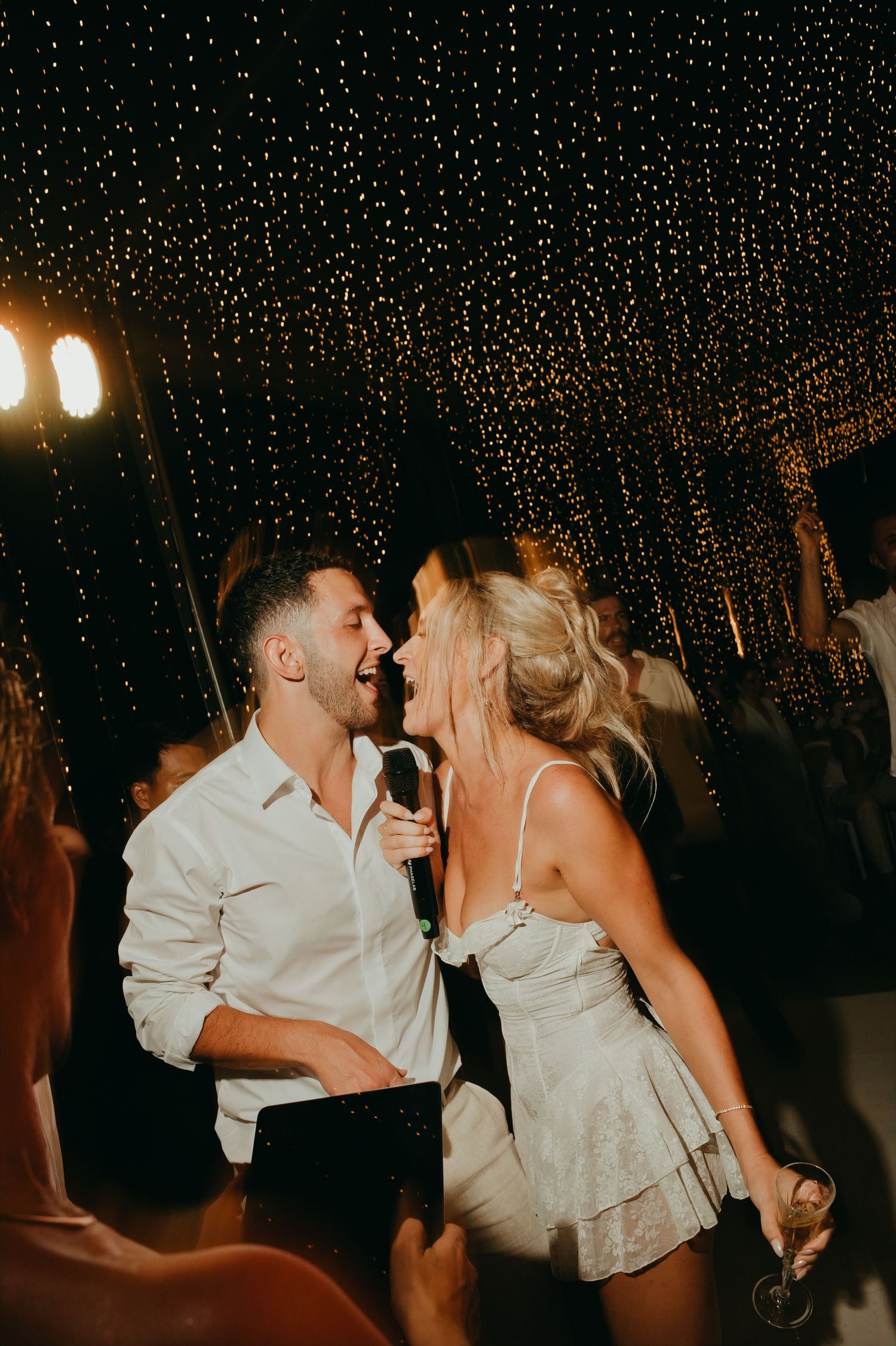 Bride and groom share a romantic moment singing together on the dance floor under fairy lights.