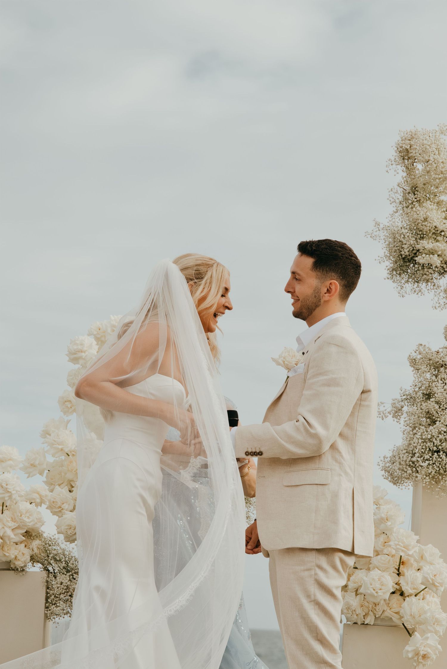 Bride and groom exchange vows outdoors surrounded by white floral arrangements at an elegant wedding ceremony.
