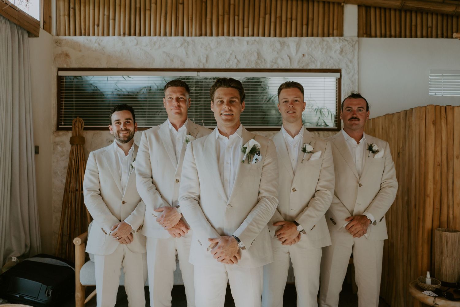 Groom and groomsmen posing in matching beige suits inside a rustic wooden venue before the wedding ceremony.