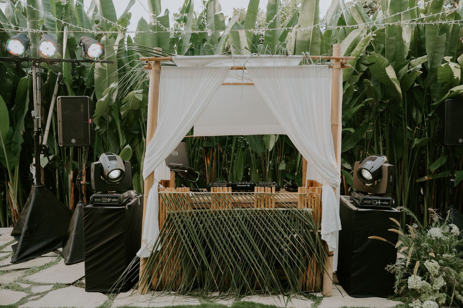 Elegant bamboo DJ booth with white drapes set up in tropical garden wedding.