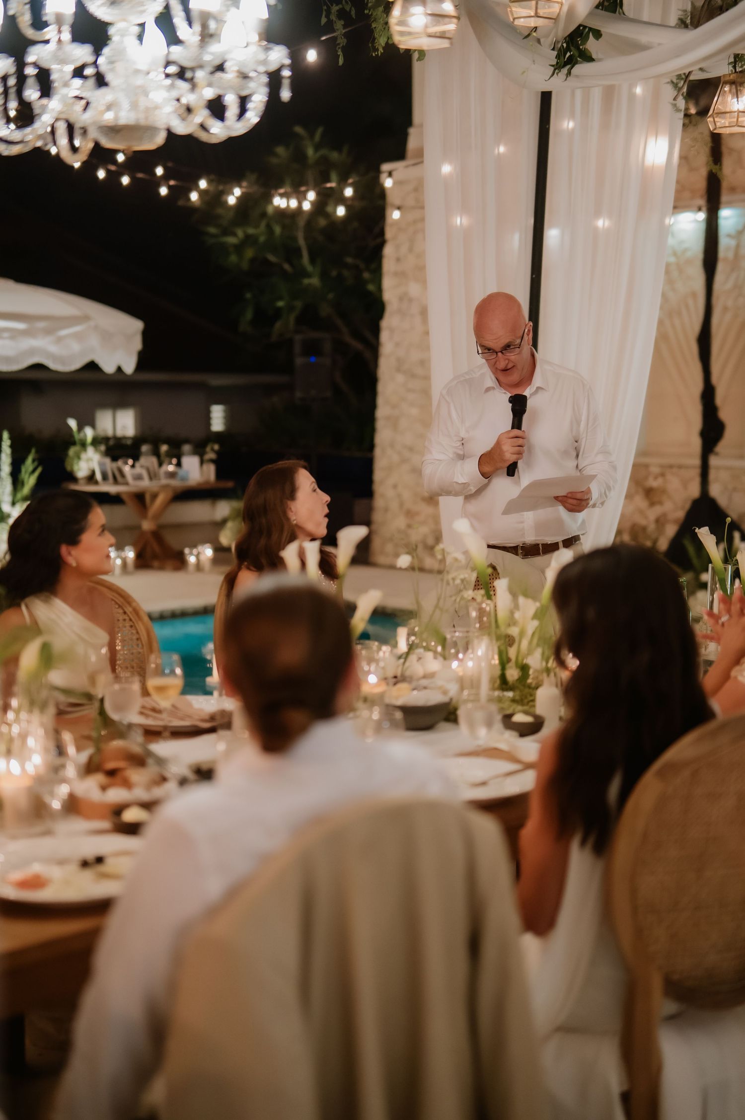 Father of the bride delivers a heartfelt speech to guests at an outdoor candlelit wedding reception.
