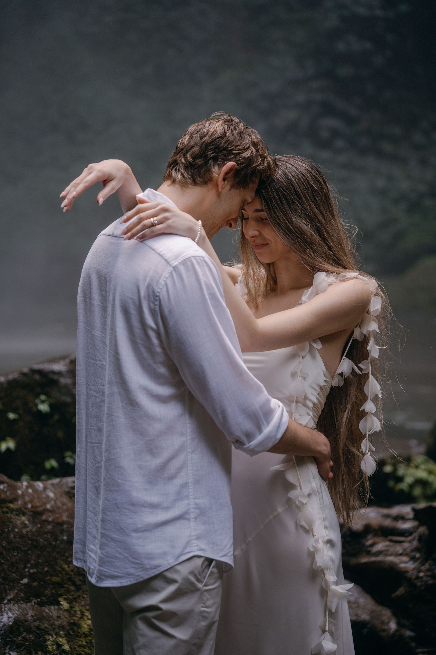 A romantic couple embraces in a dreamy outdoor setting with misty mountains in the background.