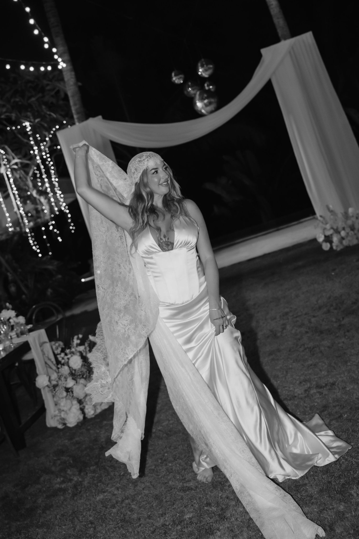 Black and white photo of bride dancing dramatically in silk gown and lace veil at night.