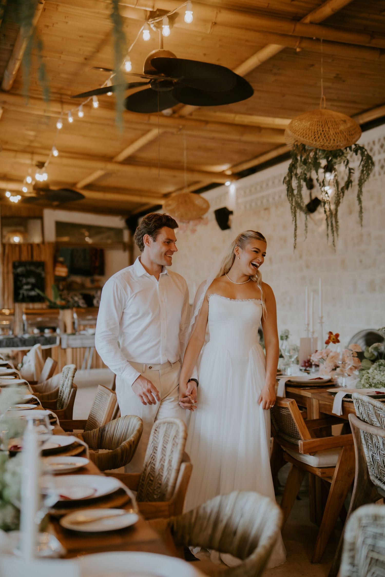 Bride and groom walk hand in hand through elegantly decorated rustic wooden reception hall.