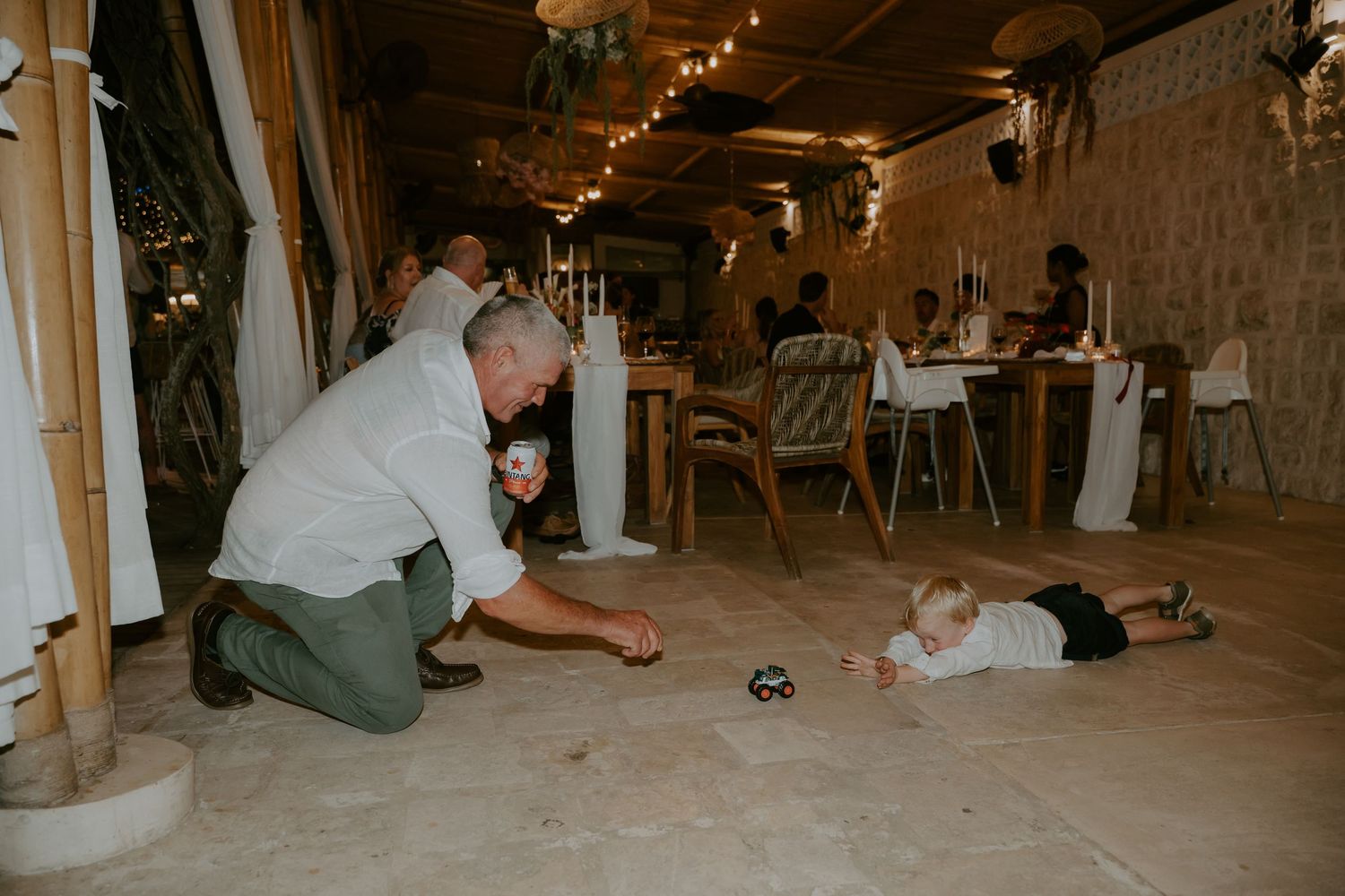 Man playing with a young child on the floor at an indoor wedding reception venue.