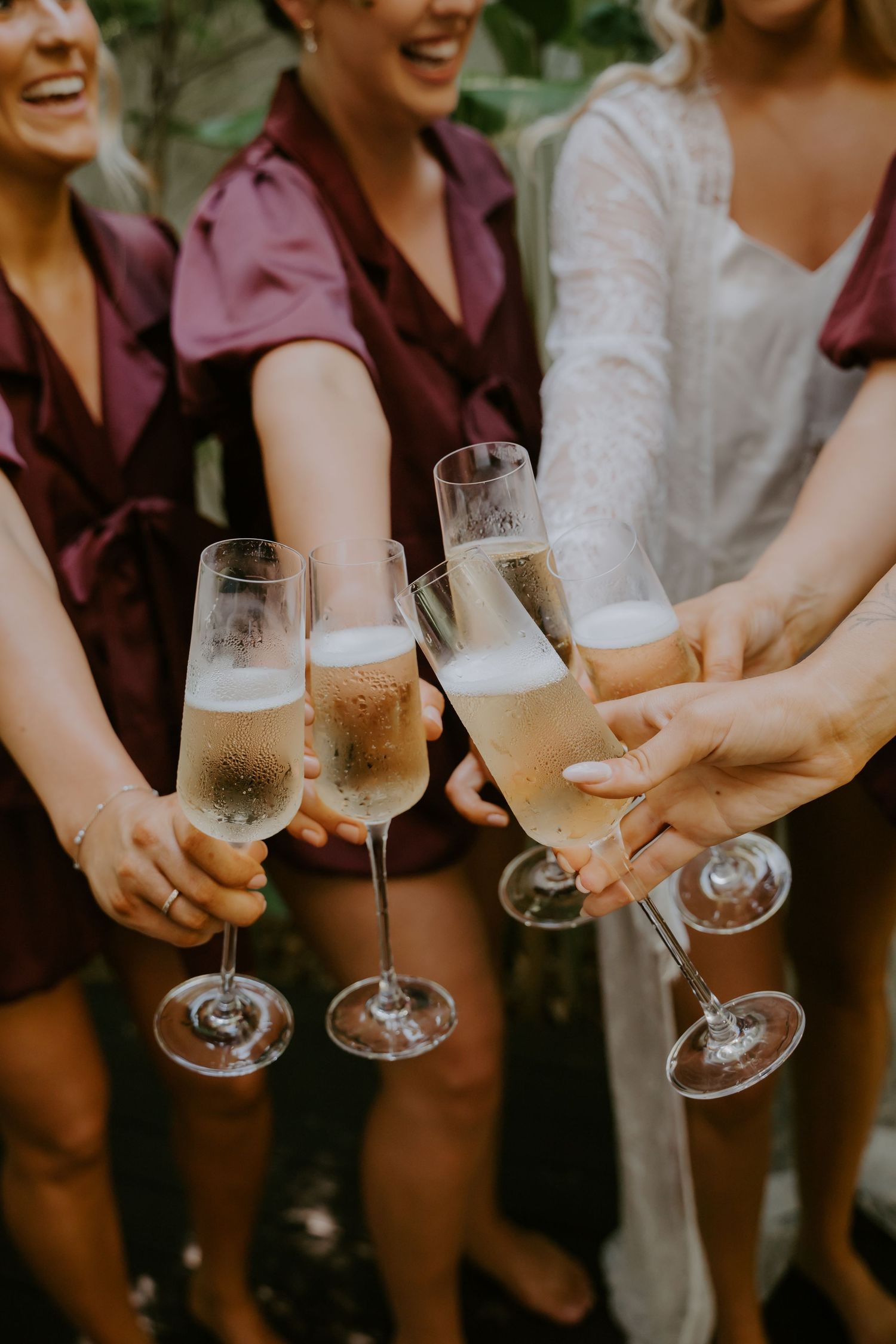 Bridesmaids in burgundy robes and bride toasting with champagne flutes at a wedding celebration.