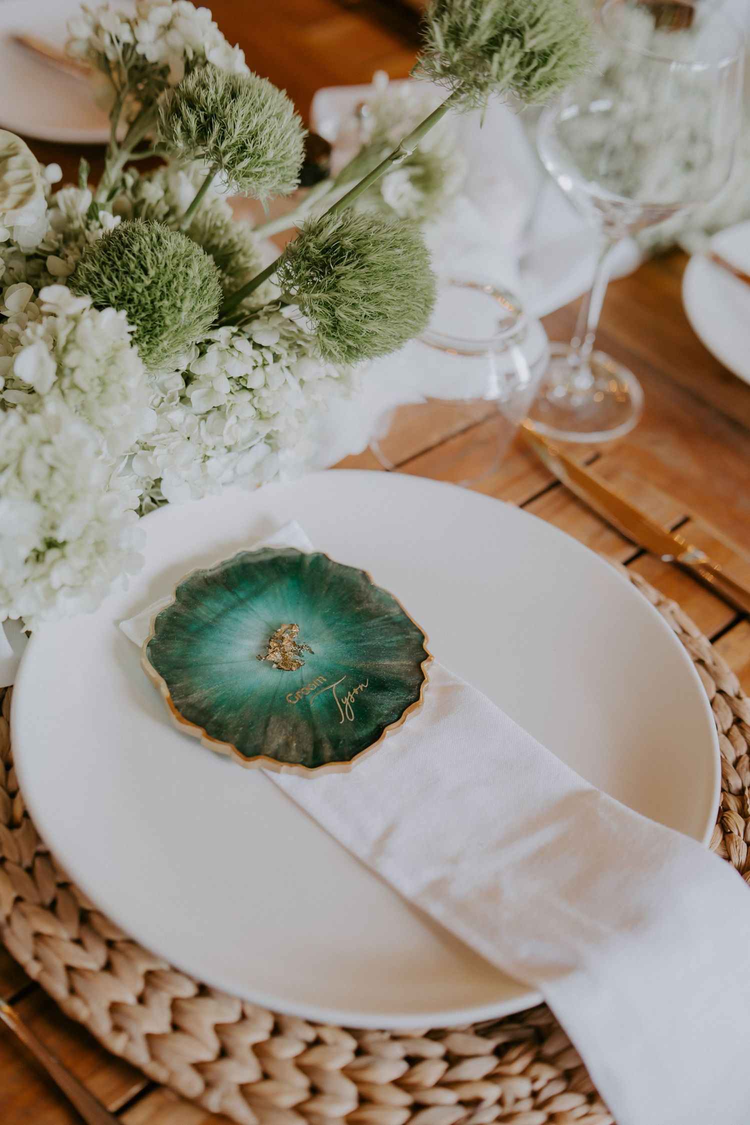 Elegant wedding place setting with green agate stone card holder, white plate, linen napkin, and floral centerpiece.