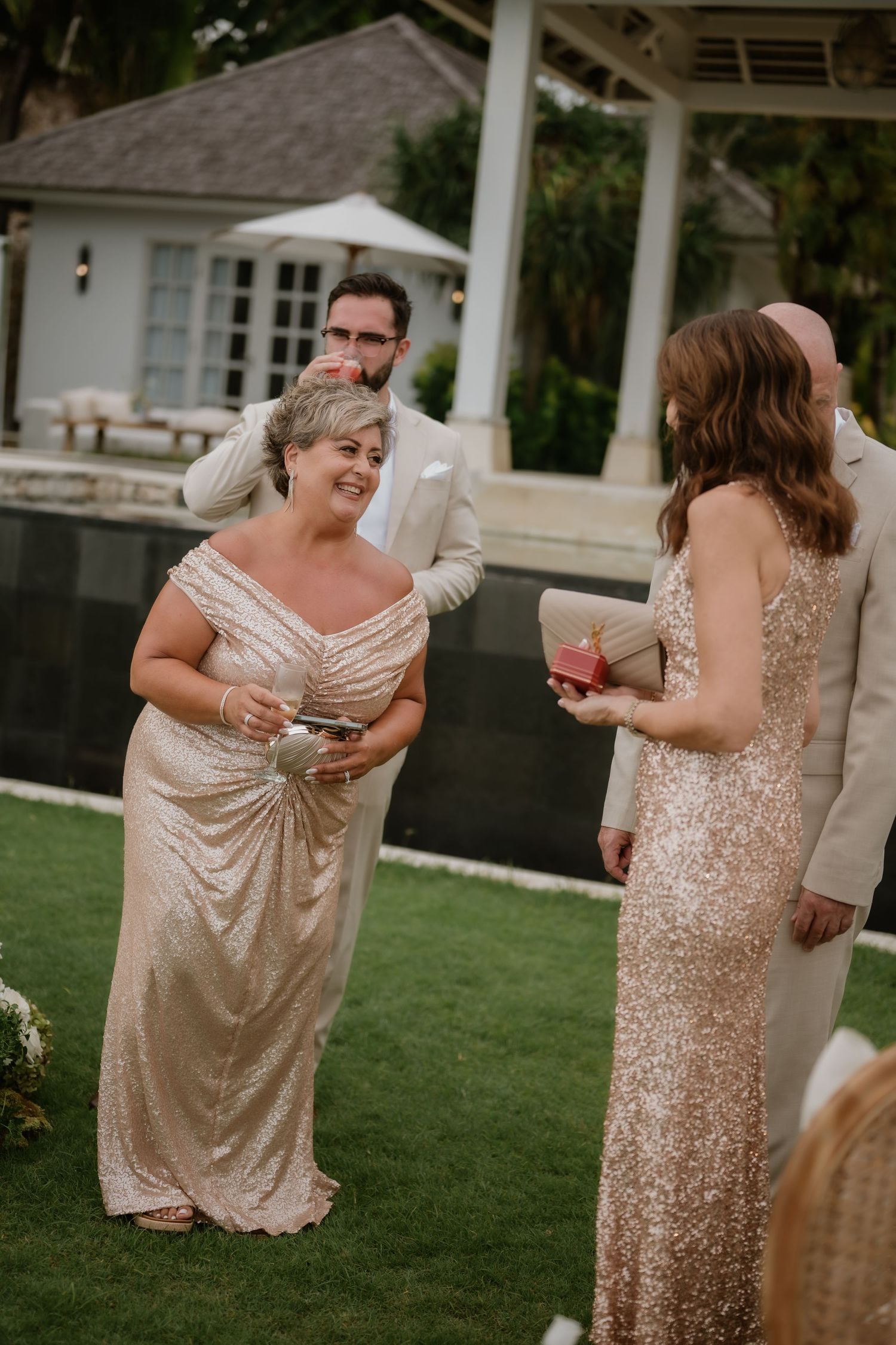 Wedding guests in gold sequin gowns socializing outdoors at a tropical venue during a reception.