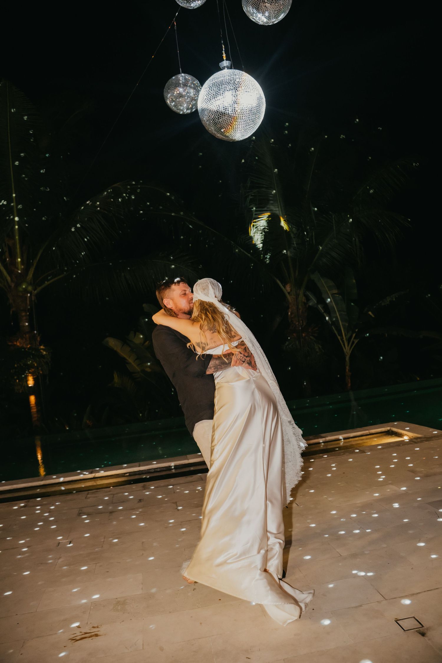 Bride and groom share a romantic first dance kiss under sparkling disco balls at their outdoor night wedding.