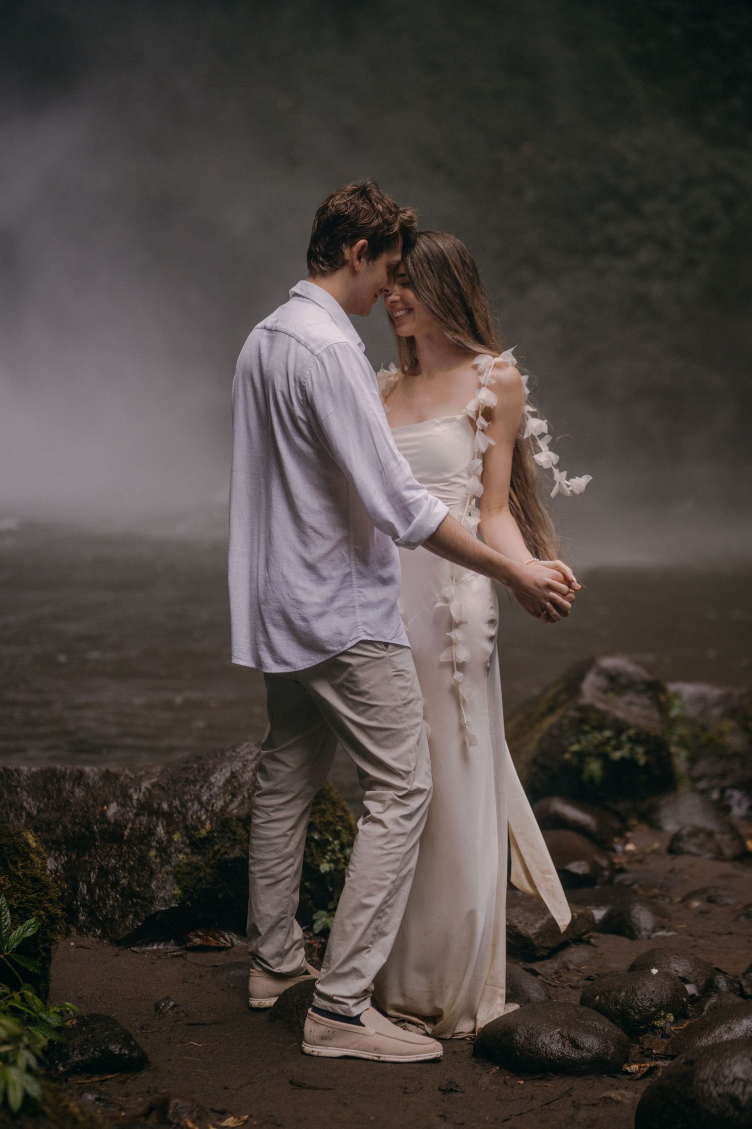 A romantic couple in white clothing embraces on a misty rocky shore in a series of intimate moments.