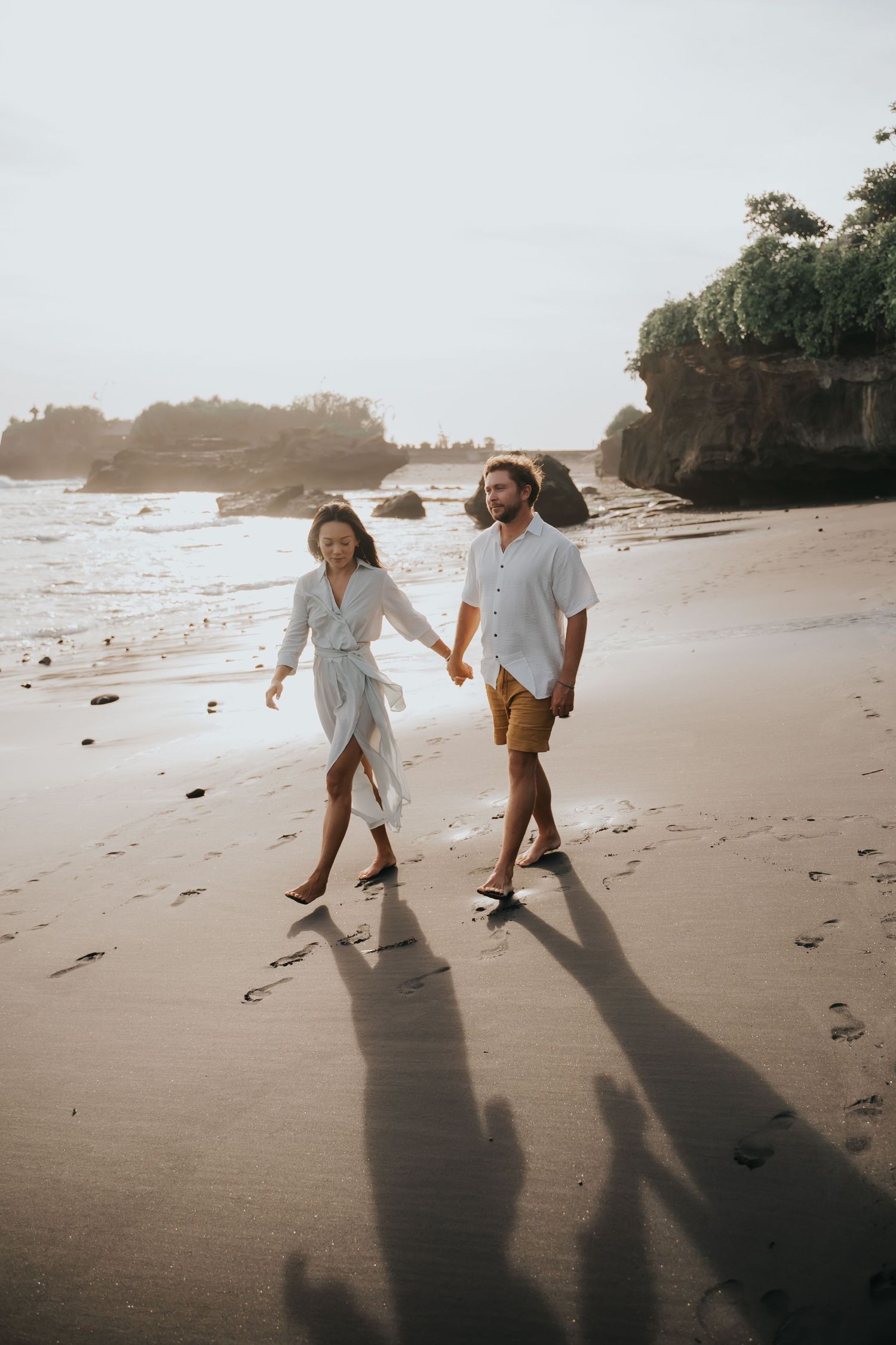 Two people dance playfully together on a sandy beach at sunset casting long shadows on the sand.