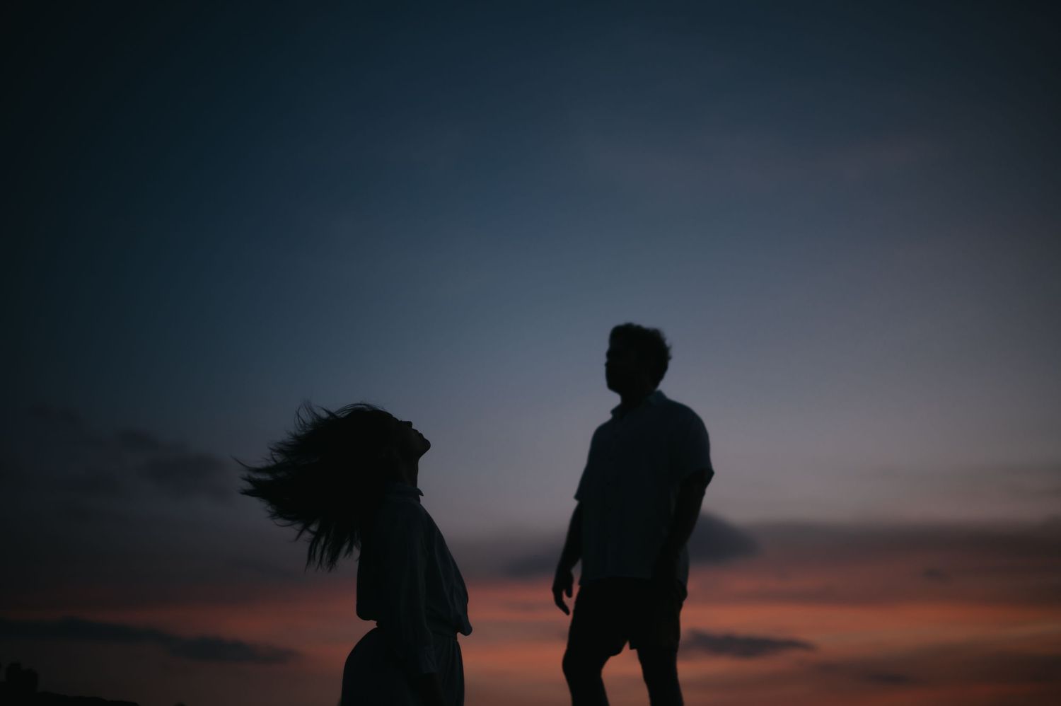 Silhouettes of people dancing against a dramatic sunset sky with vibrant orange and purple hues.