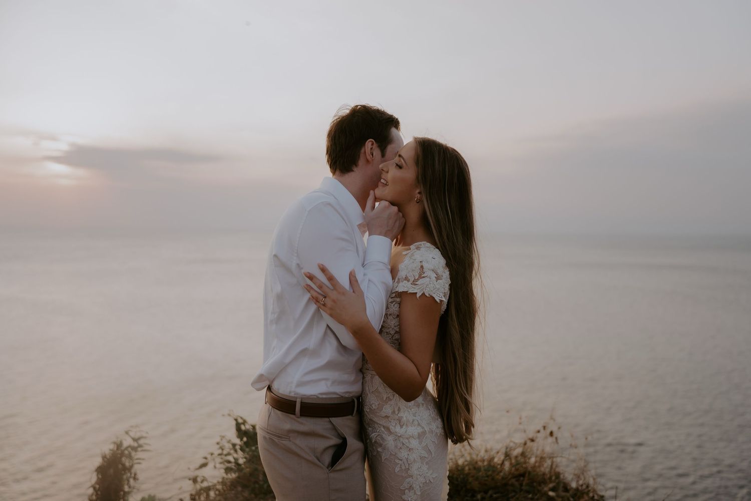 A couple shares a romantic moment at sunset on a misty beach with waves crashing in the background.