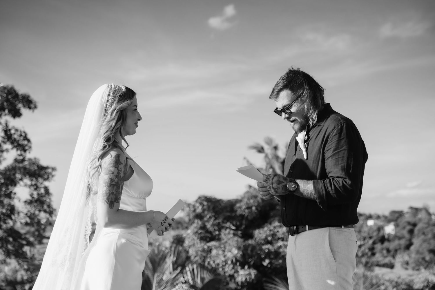 Bride and groom exchanging vows outdoors in black and white wedding ceremony photo.