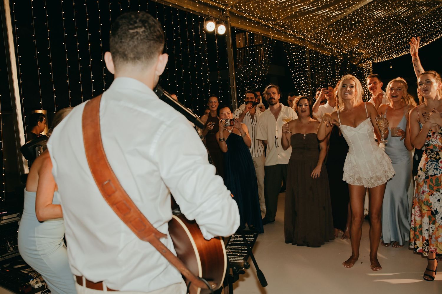 Live guitarist performing for cheering wedding guests on the dance floor at night reception.