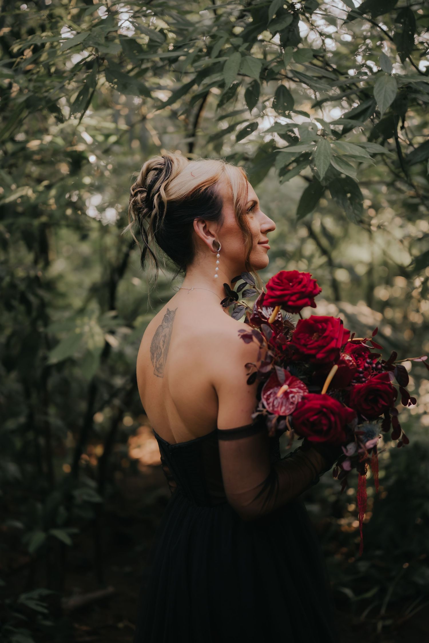 Woman in black gown holding deep red bouquet poses in lush garden setting.