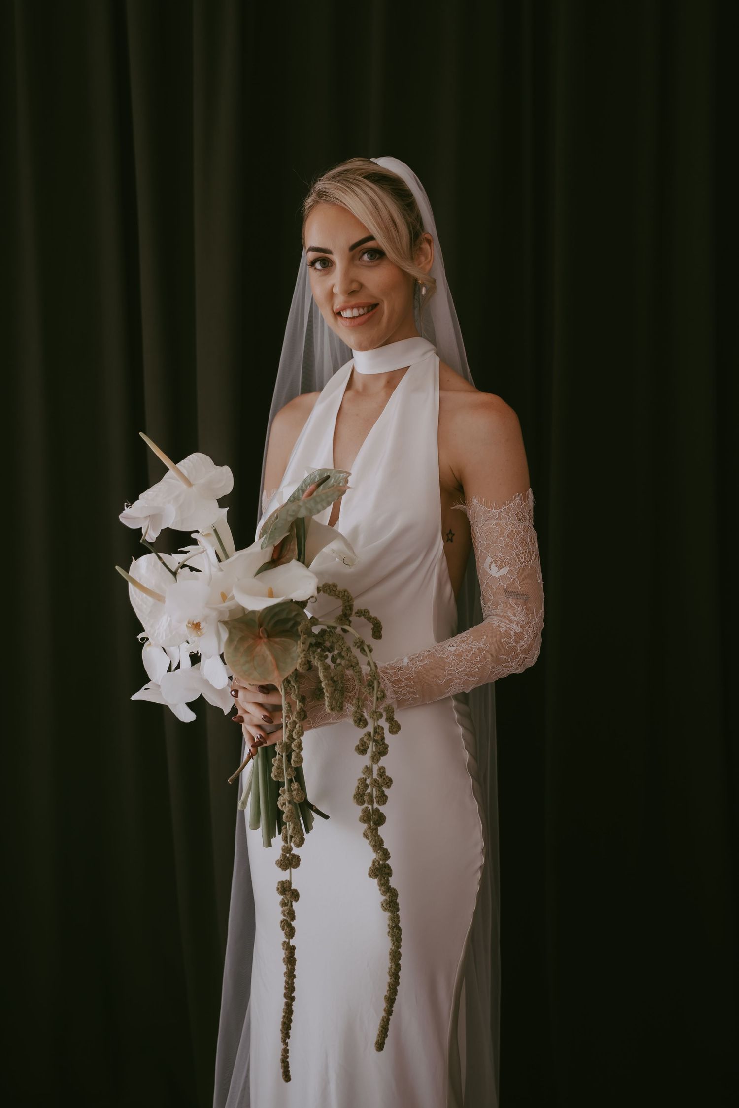 Elegant white wedding dress with cascading orchid bouquet against dark background.
