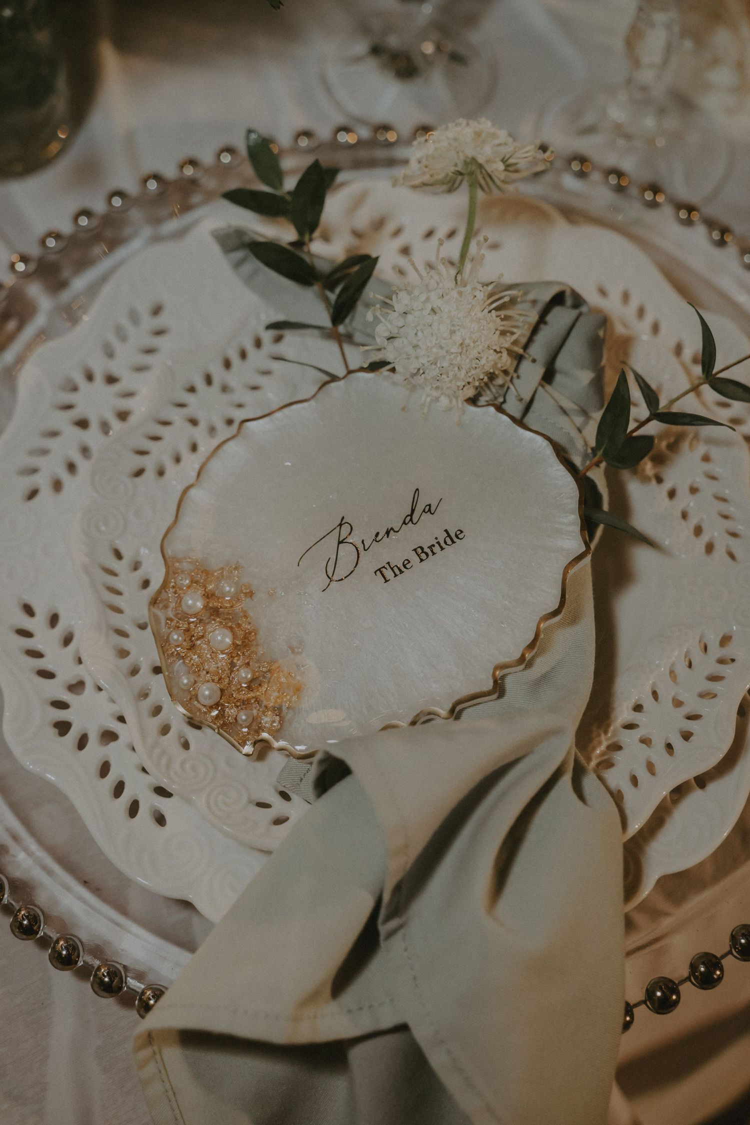 Elegant wedding place cards with delicate lace doilies and greenery accents on a cream-colored surface.