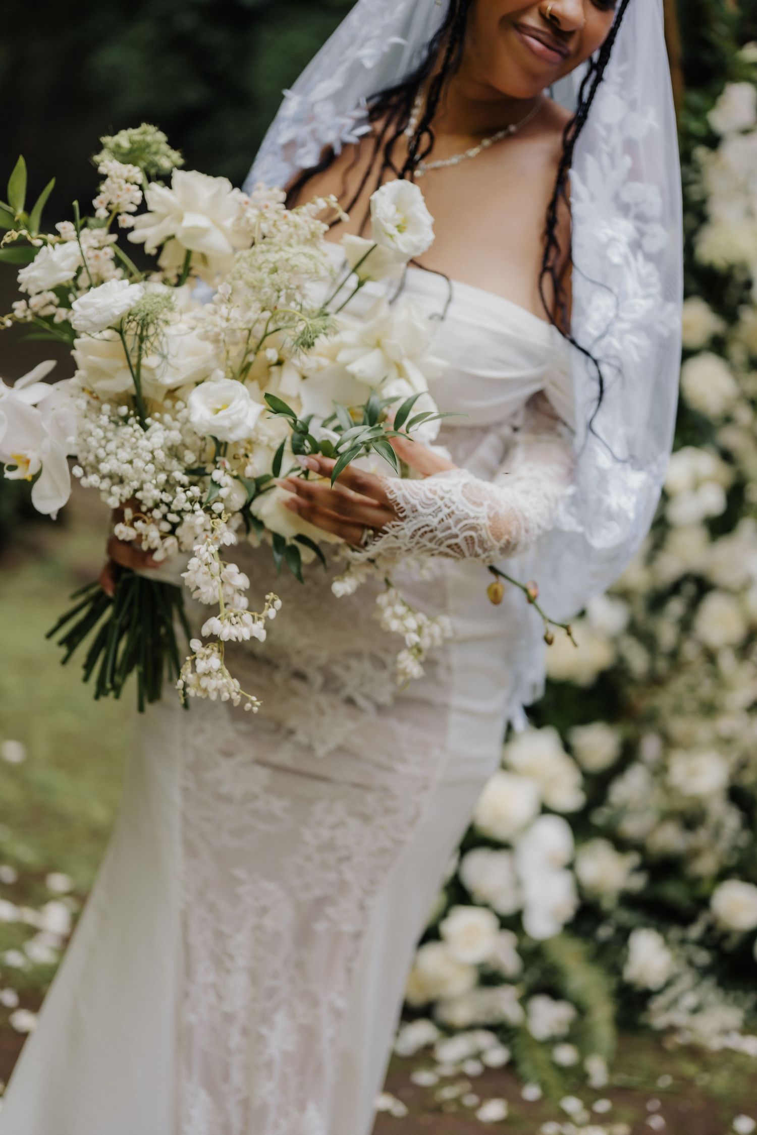 Radiant bride holding a large white bouquet of roses and baby's breath in a lace wedding gown.