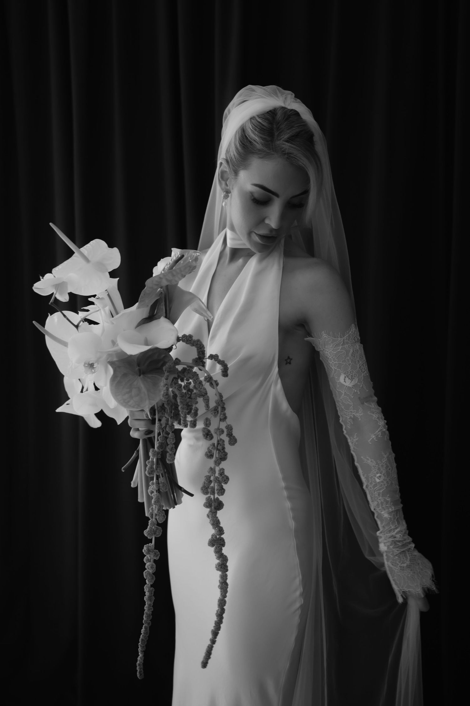 Artistic black and white portrait showcasing wedding dress and orchid bouquet details.