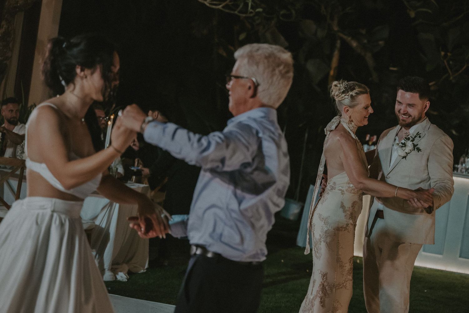 Wedding guests dance and celebrate together during an outdoor evening reception under string lights.