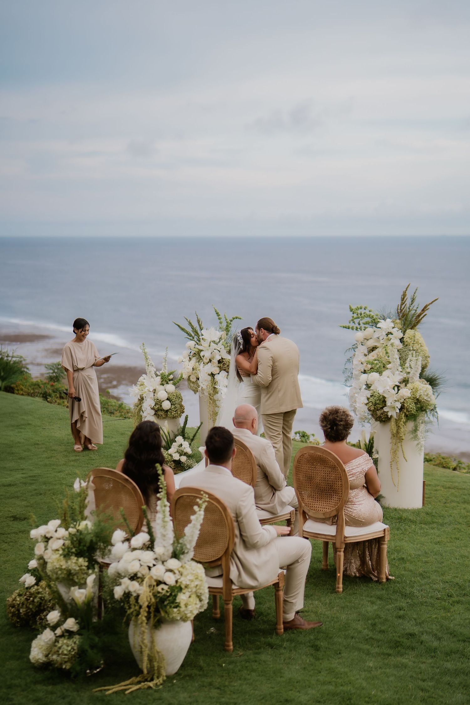 Small intimate wedding ceremony with couple kissing at floral altar overlooking a stunning ocean view.