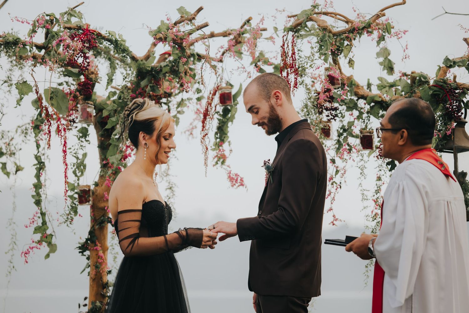 Wedding ceremony setup with floral arch and red rose petals scattered on white floor.