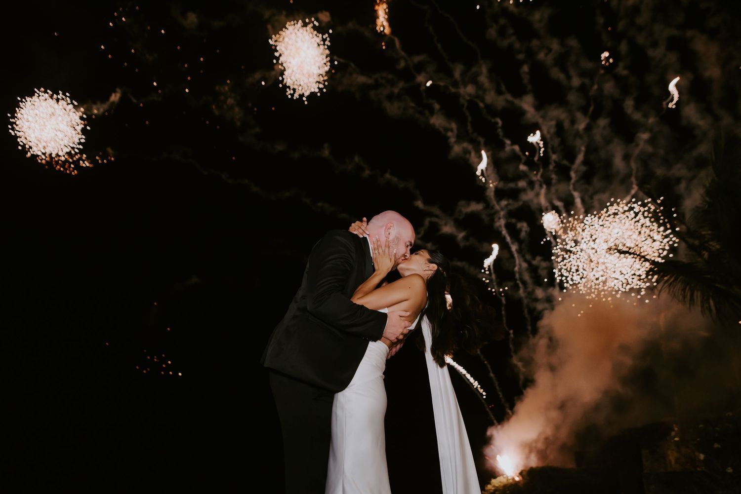 A series of firework explosions lighting up the dark night sky with bright white bursts and sparkling trails.