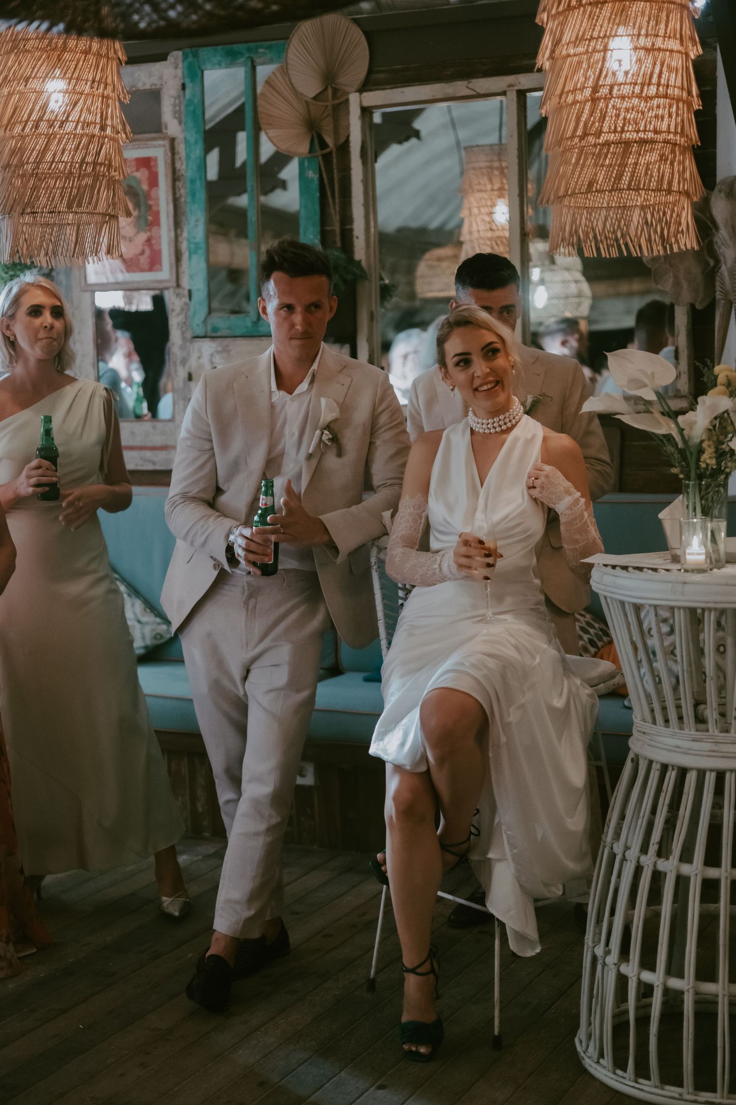 Wedding party enjoying drinks and conversation in tropical-themed venue with rattan decor.