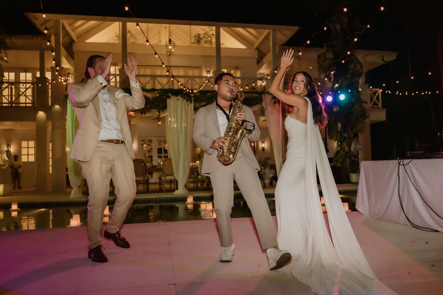 Bride dances joyfully with saxophonist and performer at vibrant outdoor wedding reception at night.