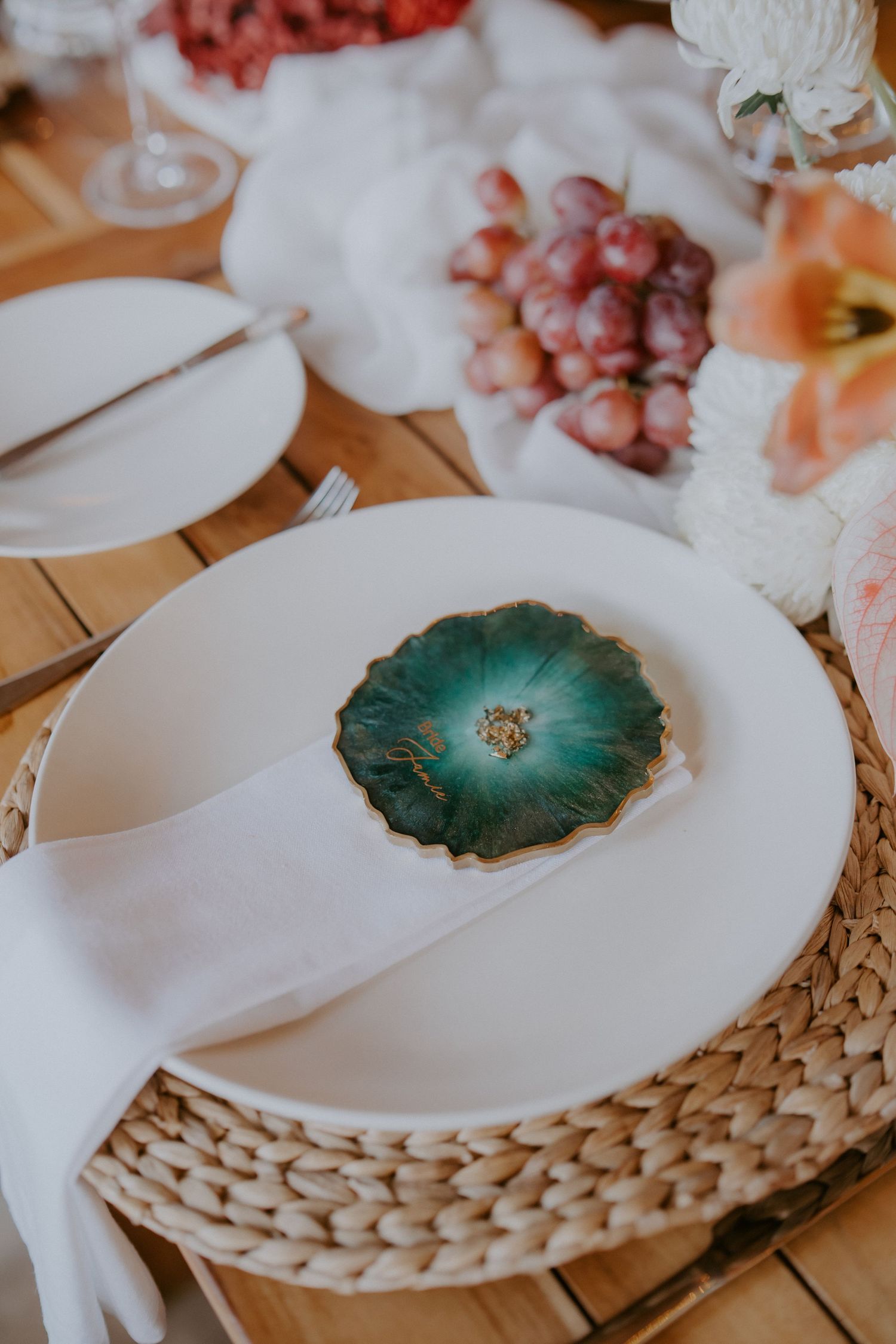 Wedding place setting with teal geode dish on white plate, linen napkin, and fresh grapes centerpiece.