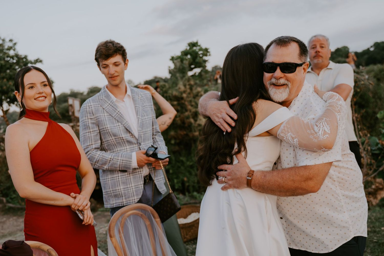 Wedding guests share warm embraces and celebrate after an outdoor cliffside ceremony at golden hour.