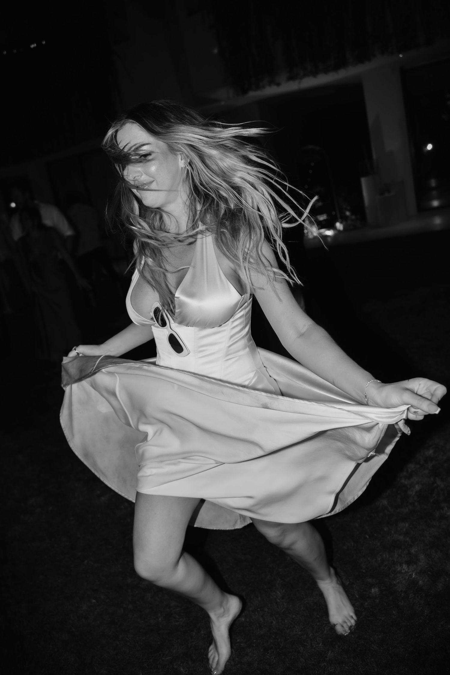 Bride twirling barefoot in white satin dress outdoors at night in black and white photo.