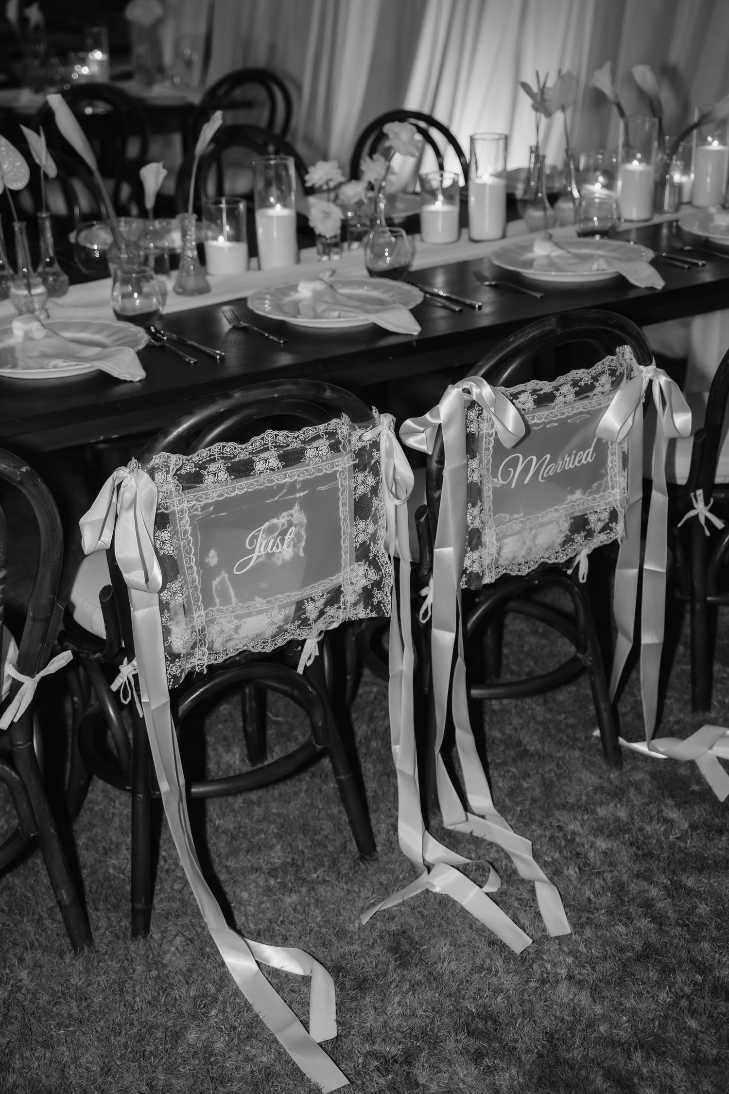 Black and white photo of Just Married chair signs with ribbon bows at an elegantly set wedding reception table.