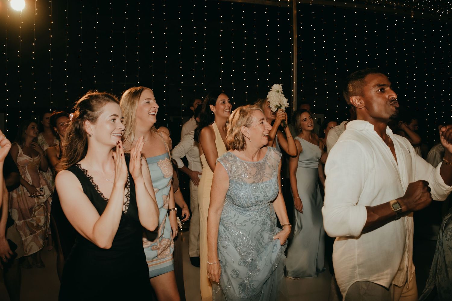 Wedding guests dancing and celebrating joyfully on the dance floor at night.