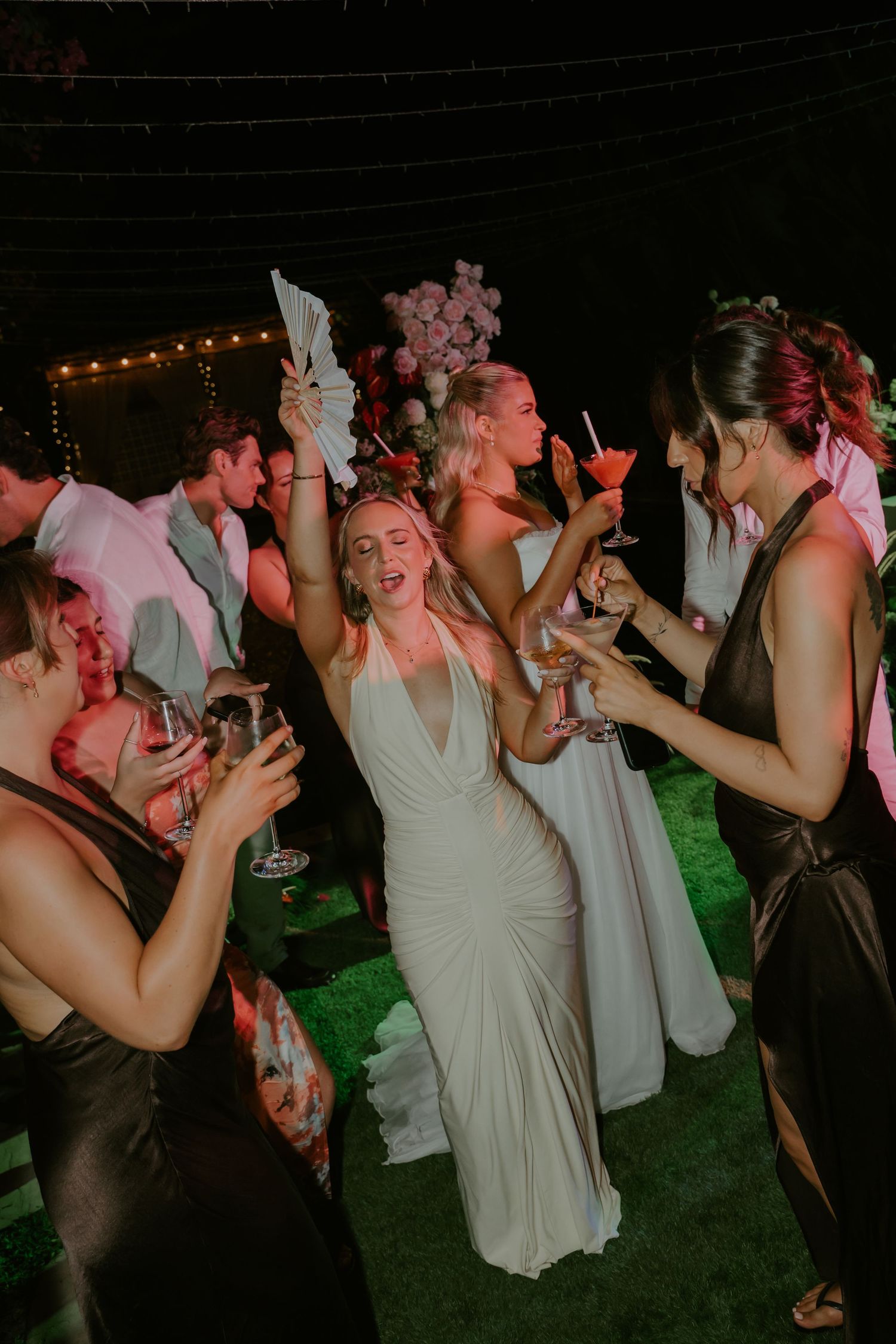 Guests in formal attire dance and celebrate with cocktails at vibrant wedding reception.