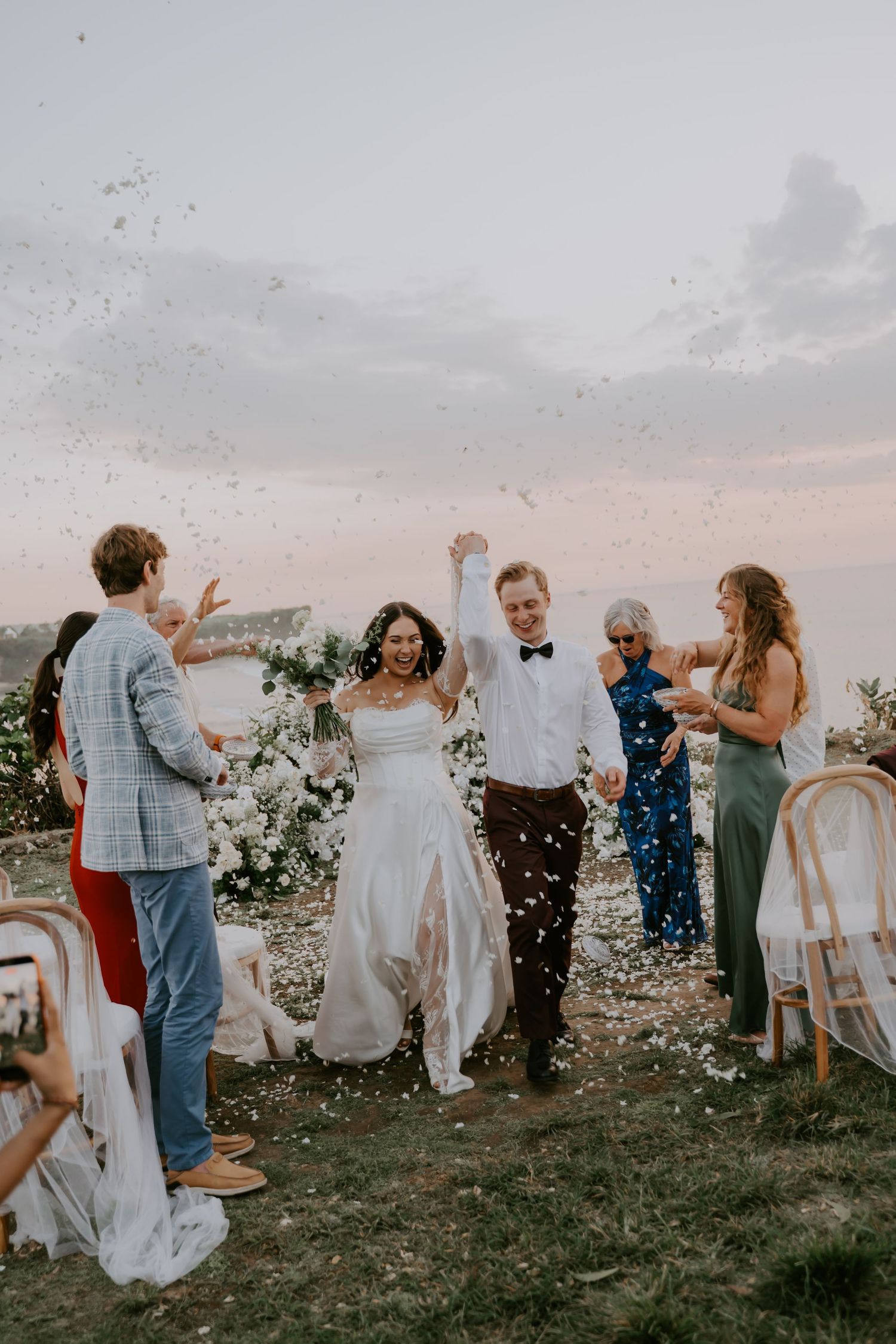 Joyful newlyweds walk through confetti shower surrounded by cheering wedding guests.